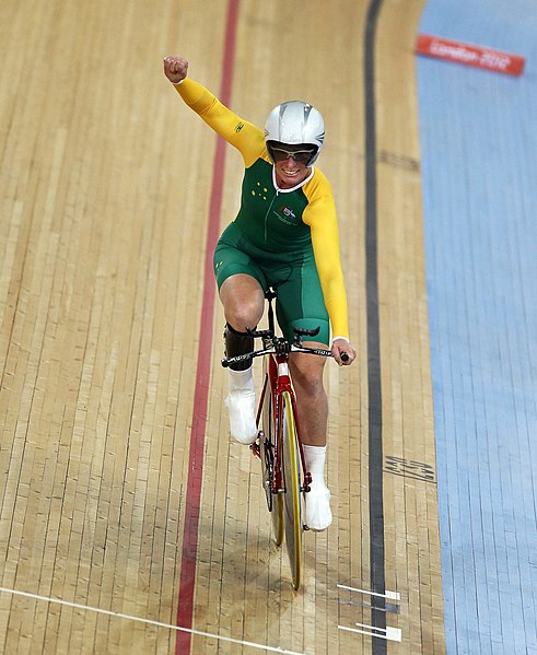 Female Para-cyclist, in green and gold attire.