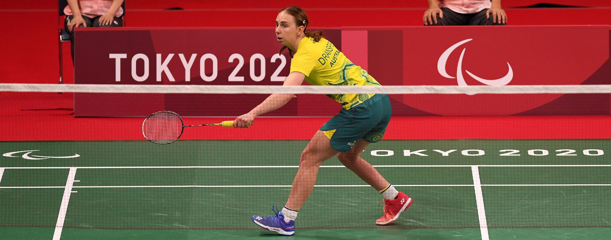 A female Australian Para-badminton player reaching for a backhand shot