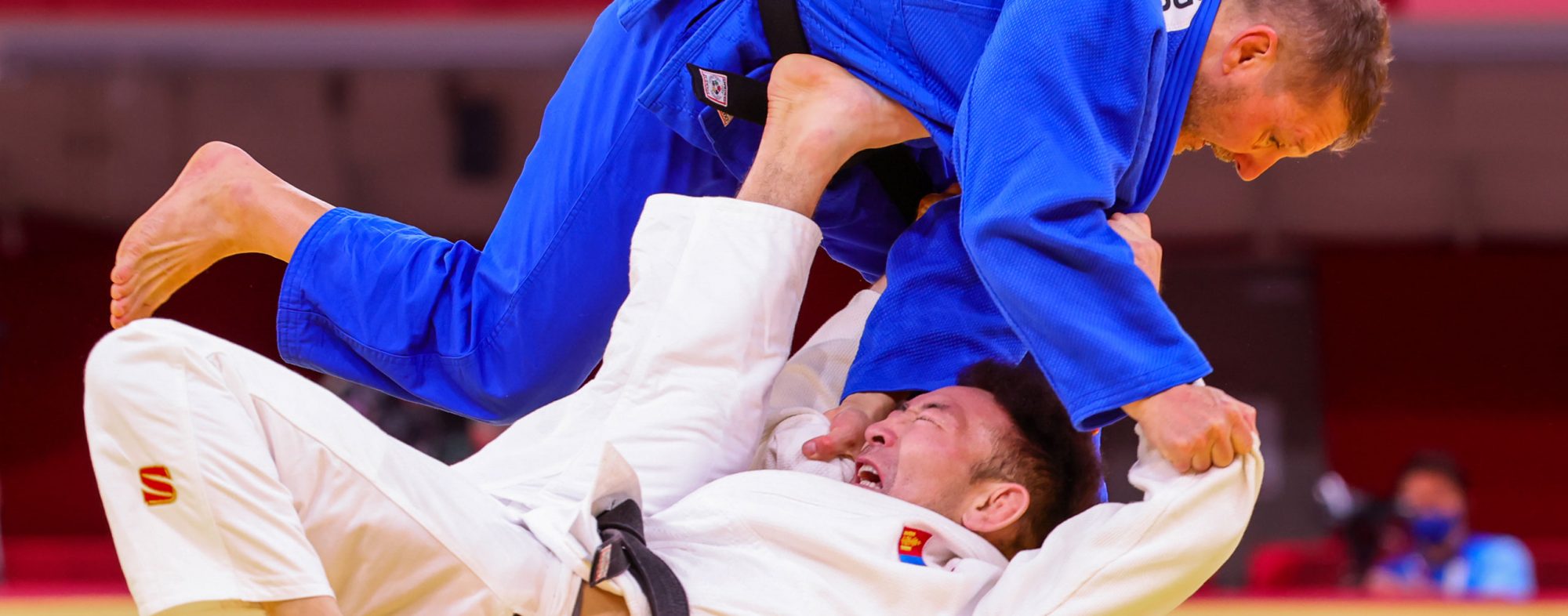 Two male Para-judo players, one is wearing blue, he is on top, the other is wearing white and is underneath