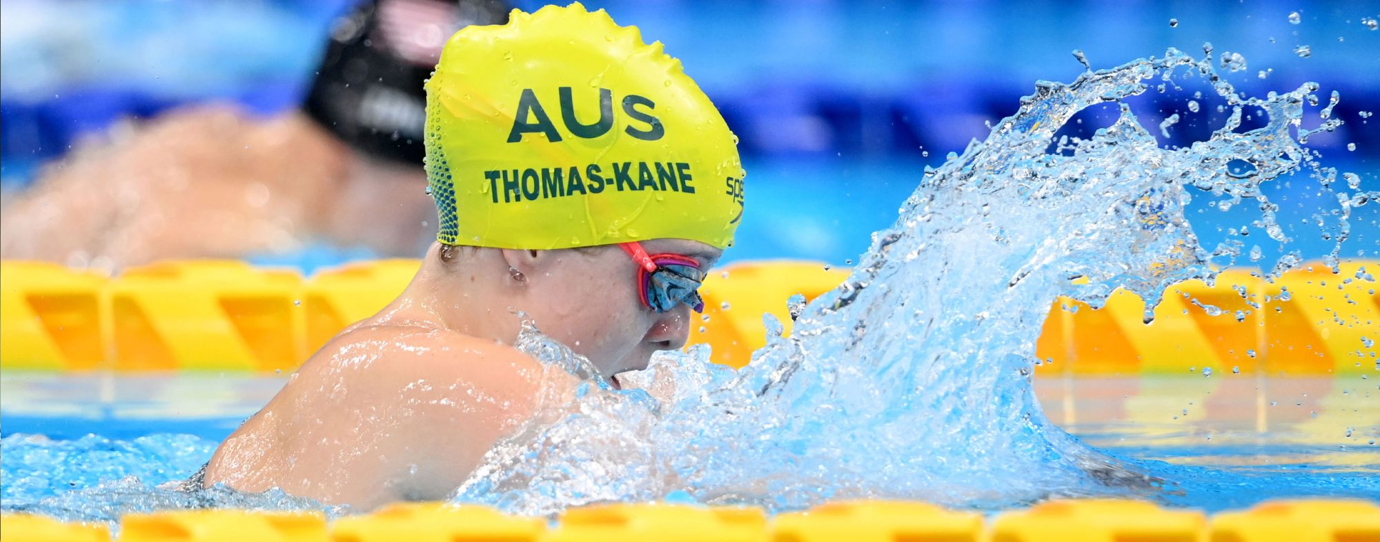 A female Para-swimmer racing in Tokyo. She is wearing a gold cap that reads: AUS, Thomas-Kane