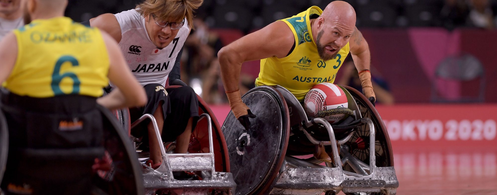 A male Australian Wheelchair rugby player with the ball in his lap competing against Japan in Tokyo