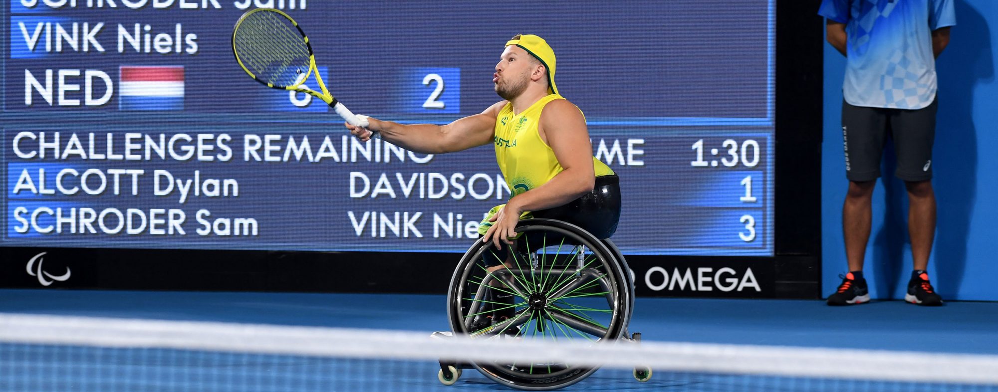 Australian Paralympian Dylan Alcott hitting a tennis ball at Tokyo 2020. He is wearing a gold cap and singlet.